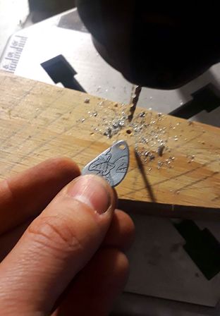 Photo d'une petite plaque de zinc gravée à côté d'une perceuse ayant servi à percer un trou dedans